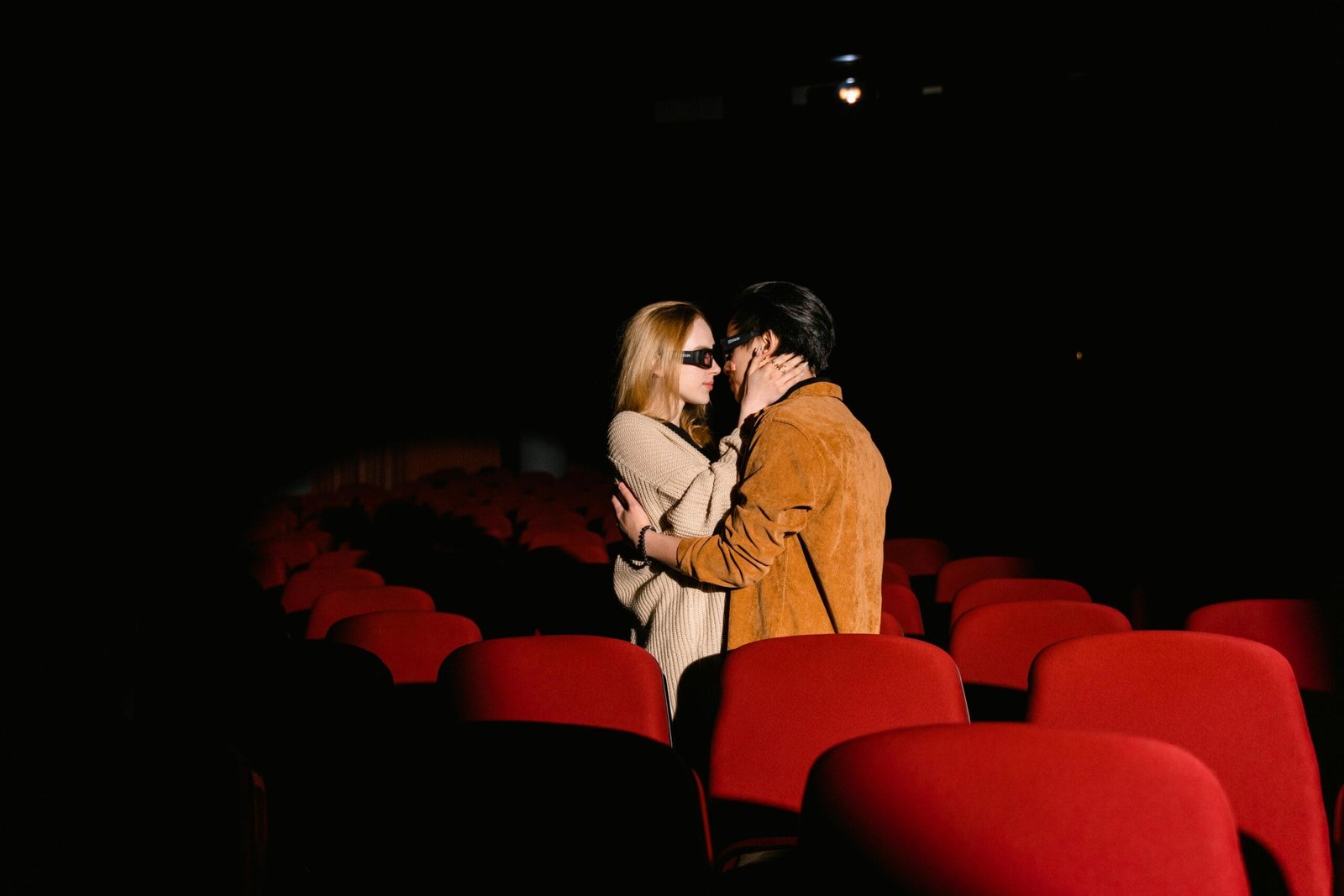 A romantic couple wearing 3D glasses embracing in an empty movie theater.