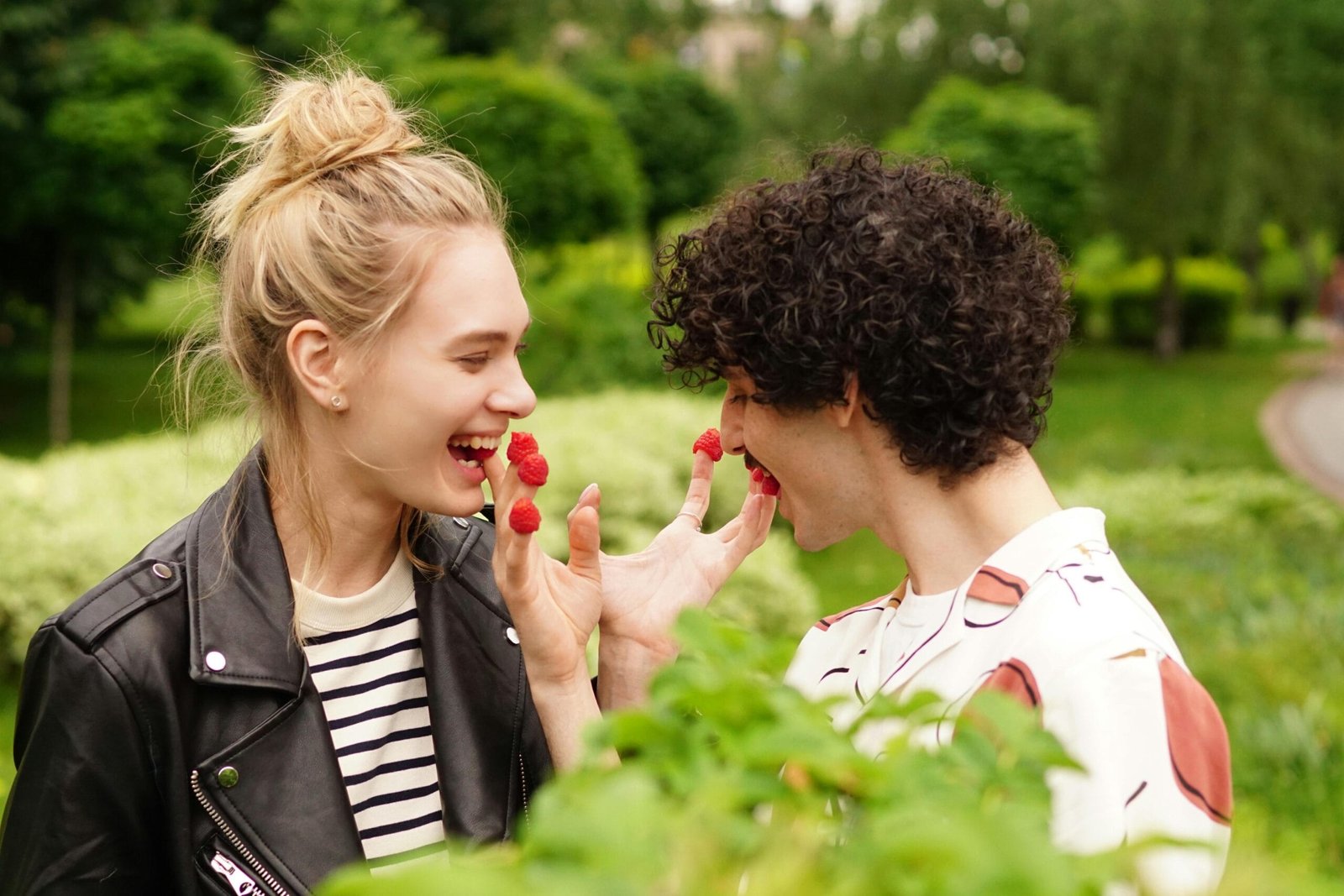 Couple having fun with raspberries in a lush green park. Love and laughter outdoors.